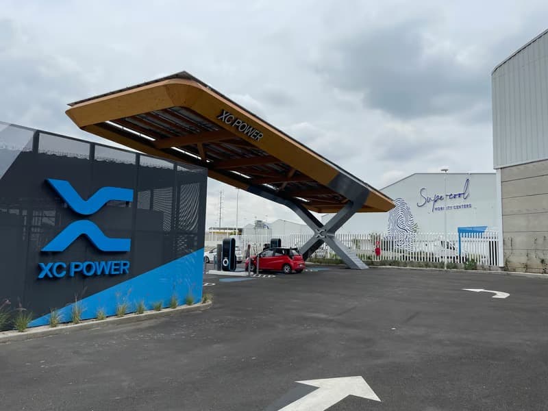 Street-level view of the XC Power entrance canopy and QiOn chargers at the Supercool Mobility Center in Puebla, Mexico, with a red electric vehicle charging underneath