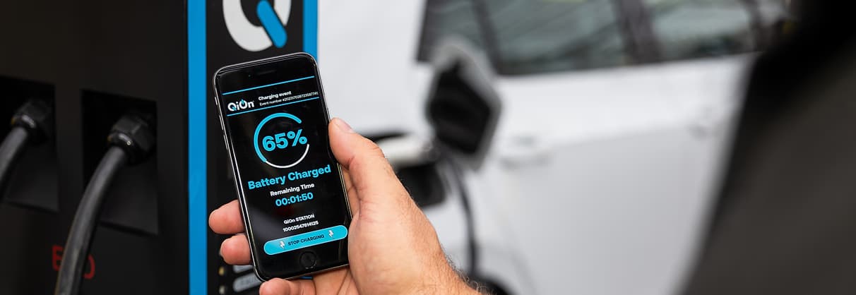 Hand holding smartphone with EV charging management app showing real-time data while electric vehicle charges, demonstrating OCPP 2.0.1 smart charging software capabilities