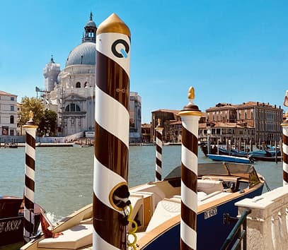 QiOn E-Dock integrated into traditional Venetian striped mooring poles on the Grand Canal with a gondola and Santa Maria della Salute basilica in the background, showing design harmony with heritage waterfront